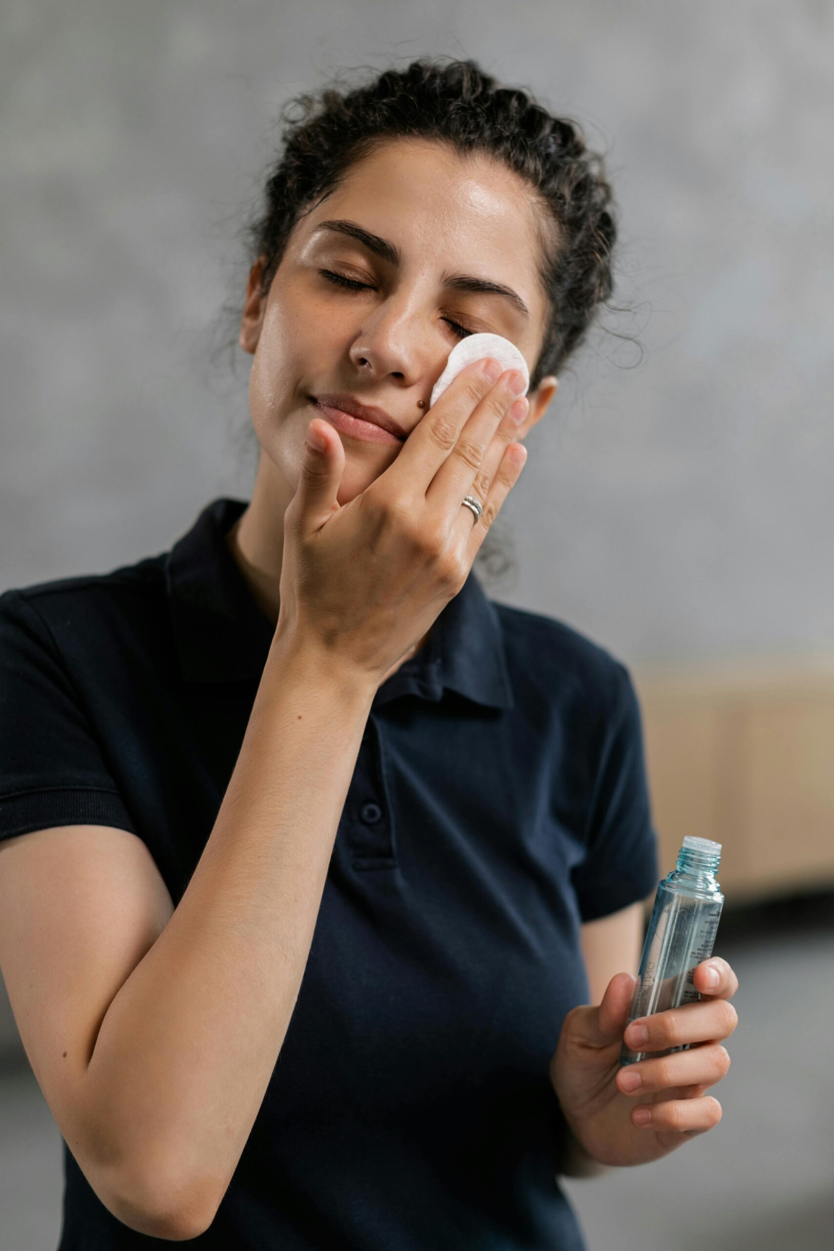Adult woman using cotton pad and toner for skincare routine indoors.